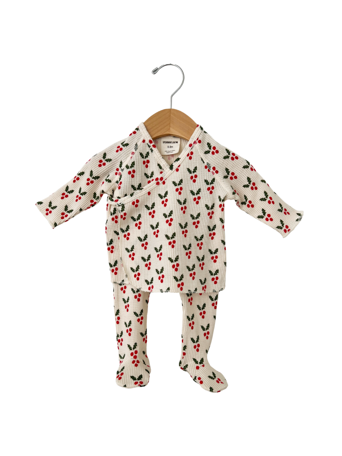 White baby outfit with red cherry pattern, hanging on a wooden hanger.