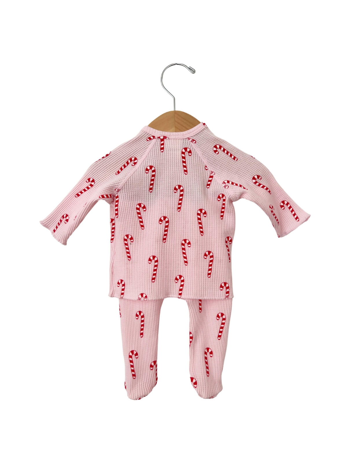 Pink children's pajamas with candy cane print, hanging on a wooden hanger against a white background.