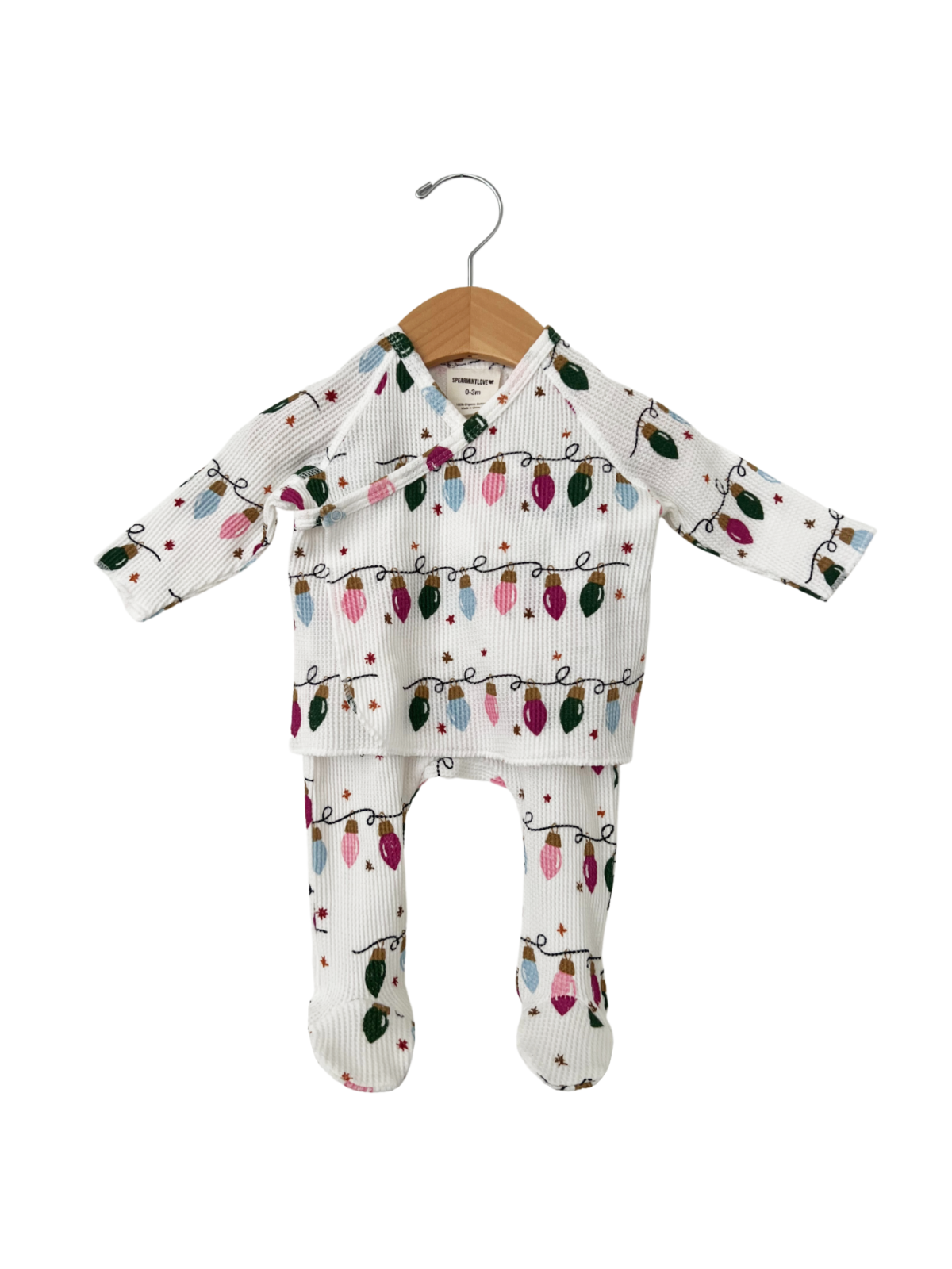 White baby outfit with festive light bulb pattern, including a long-sleeve top and matching pants, hanging on a wooden hook.