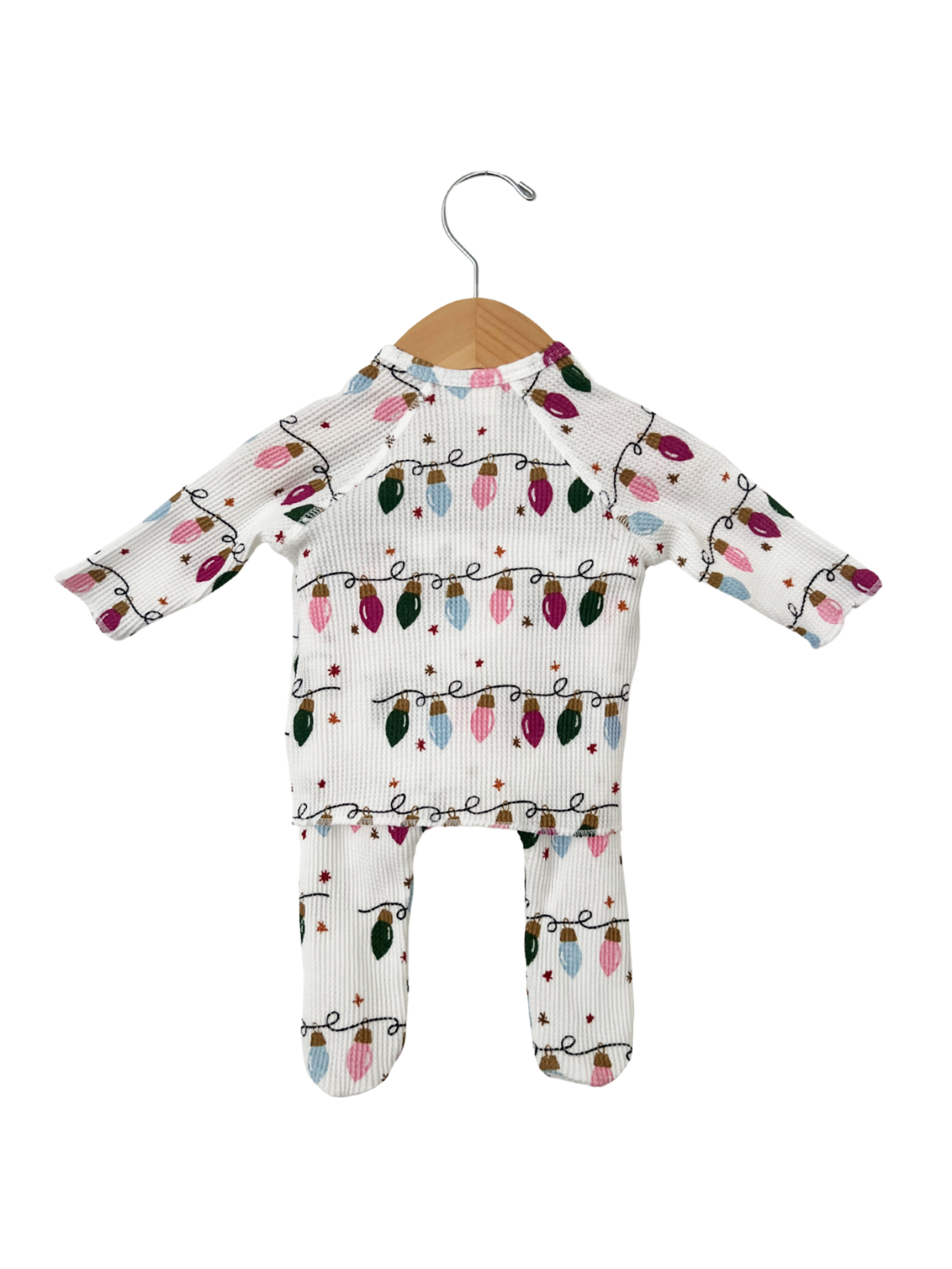 White children's outfit with colorful Christmas lights print, hanging on a wooden hanger.
