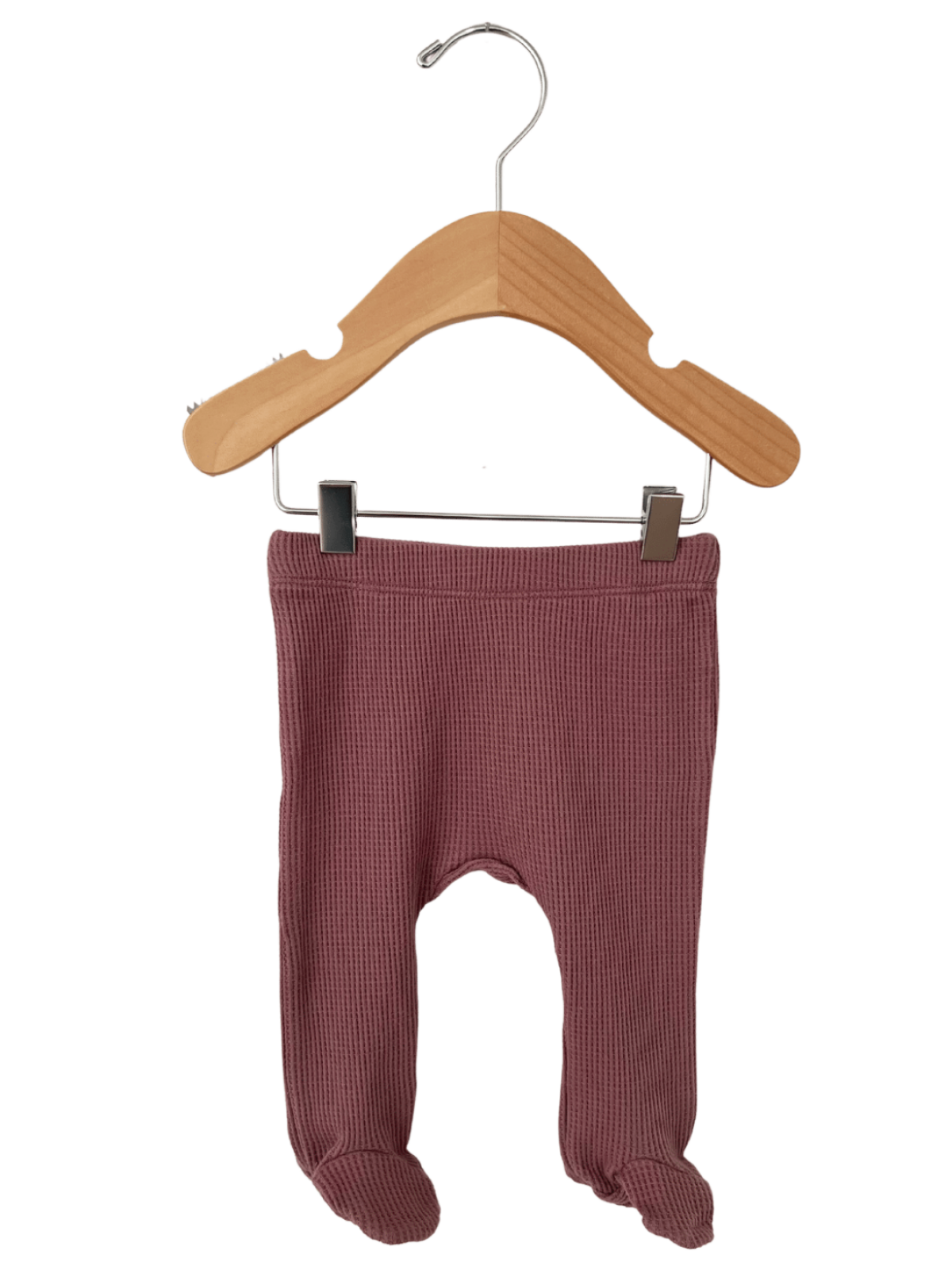 Pink baby leggings hanging on a wooden hanger, featuring footed design and ribbed texture.