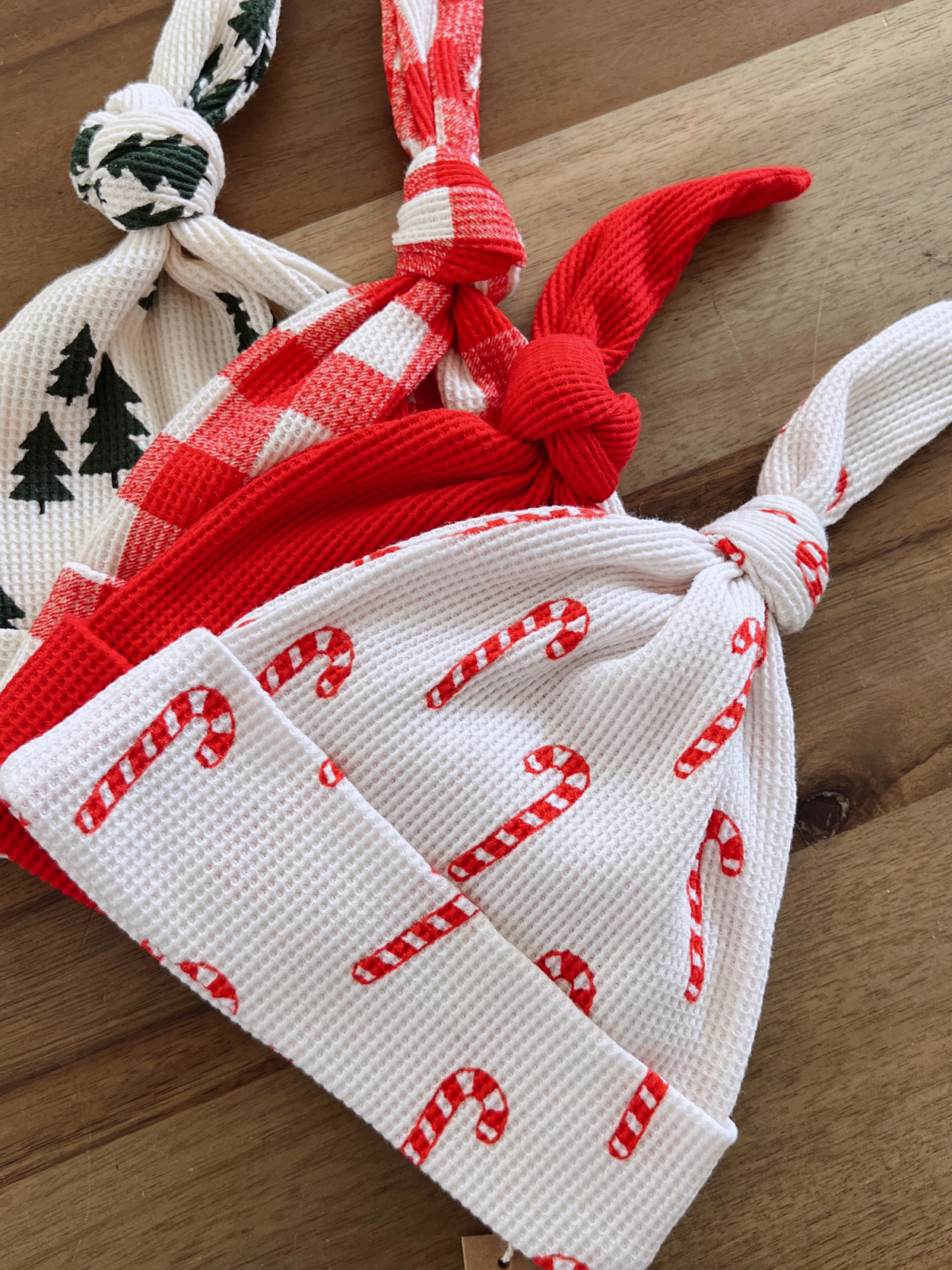 Three festive hats in red and white with candy cane and plaid patterns, displayed on a wooden surface.