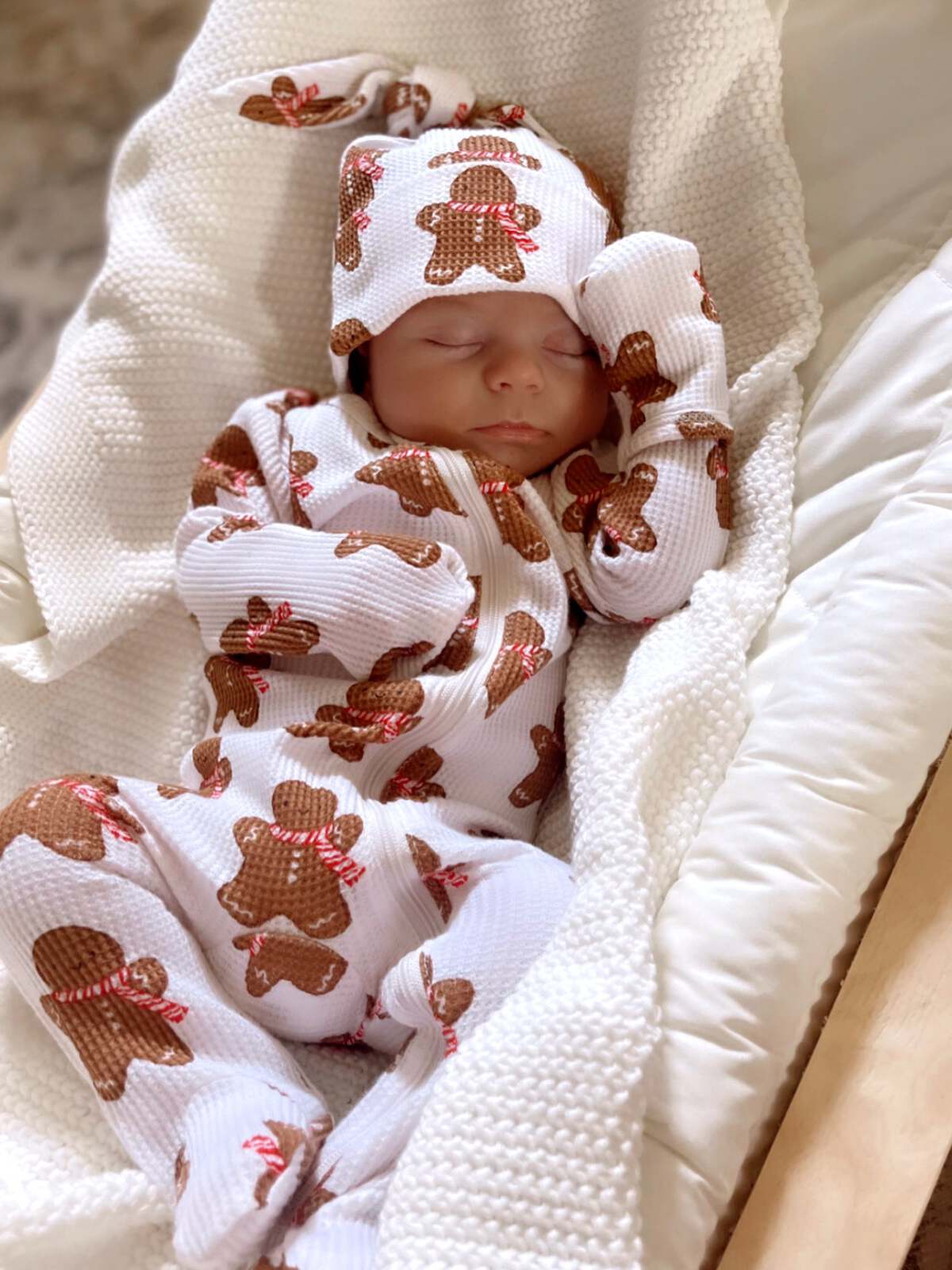 Sleeping baby in gingerbread-patterned outfit, nestled in a cozy blanket.