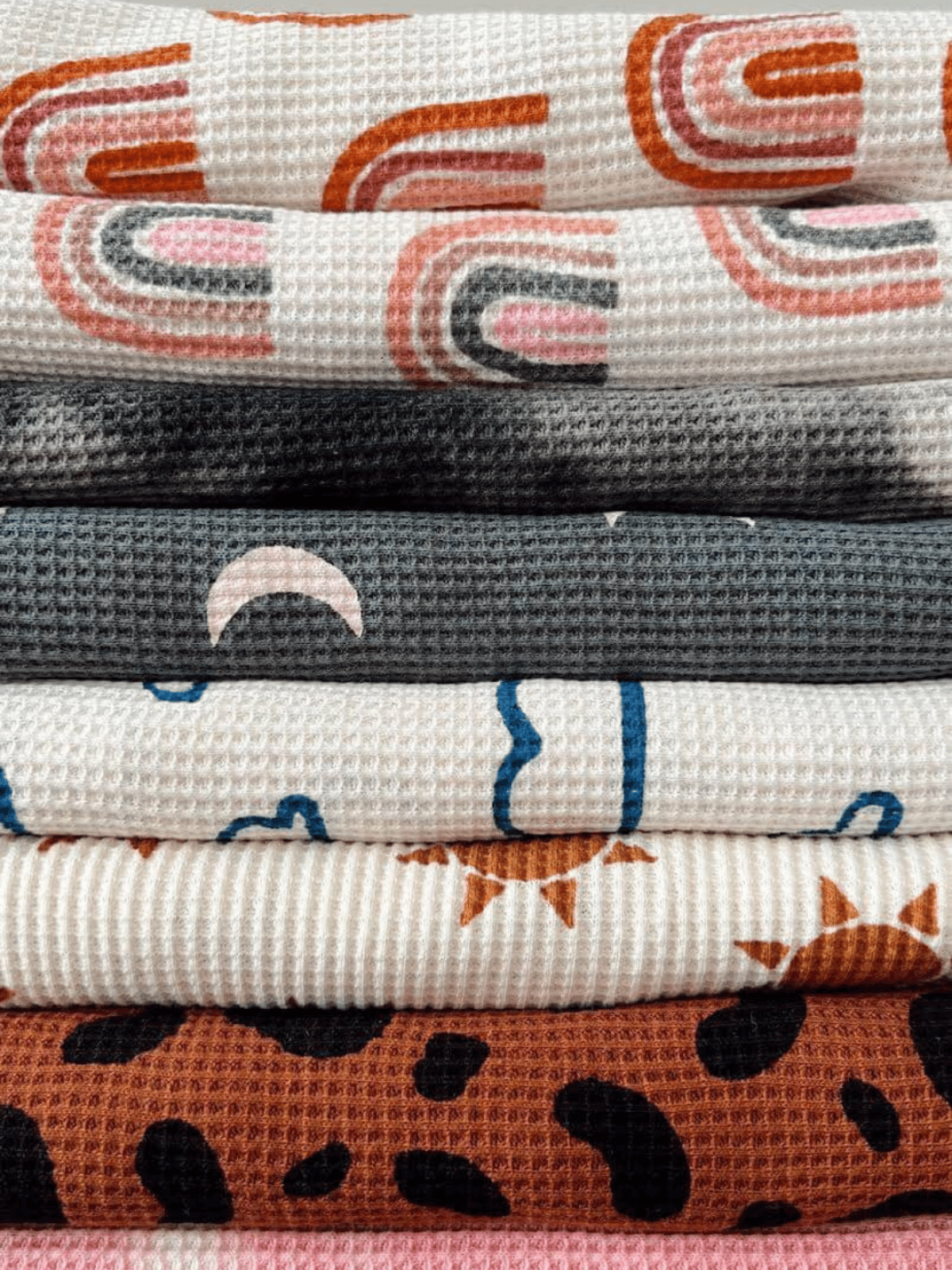 Stack of patterned fabric with designs including rainbows, moons, and leopard prints in various colors and textures.