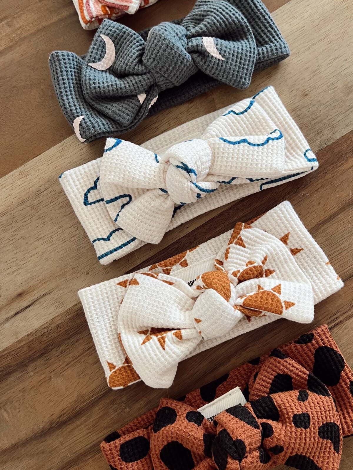 Four colorful fabric headbands with bows displayed on a wooden surface.