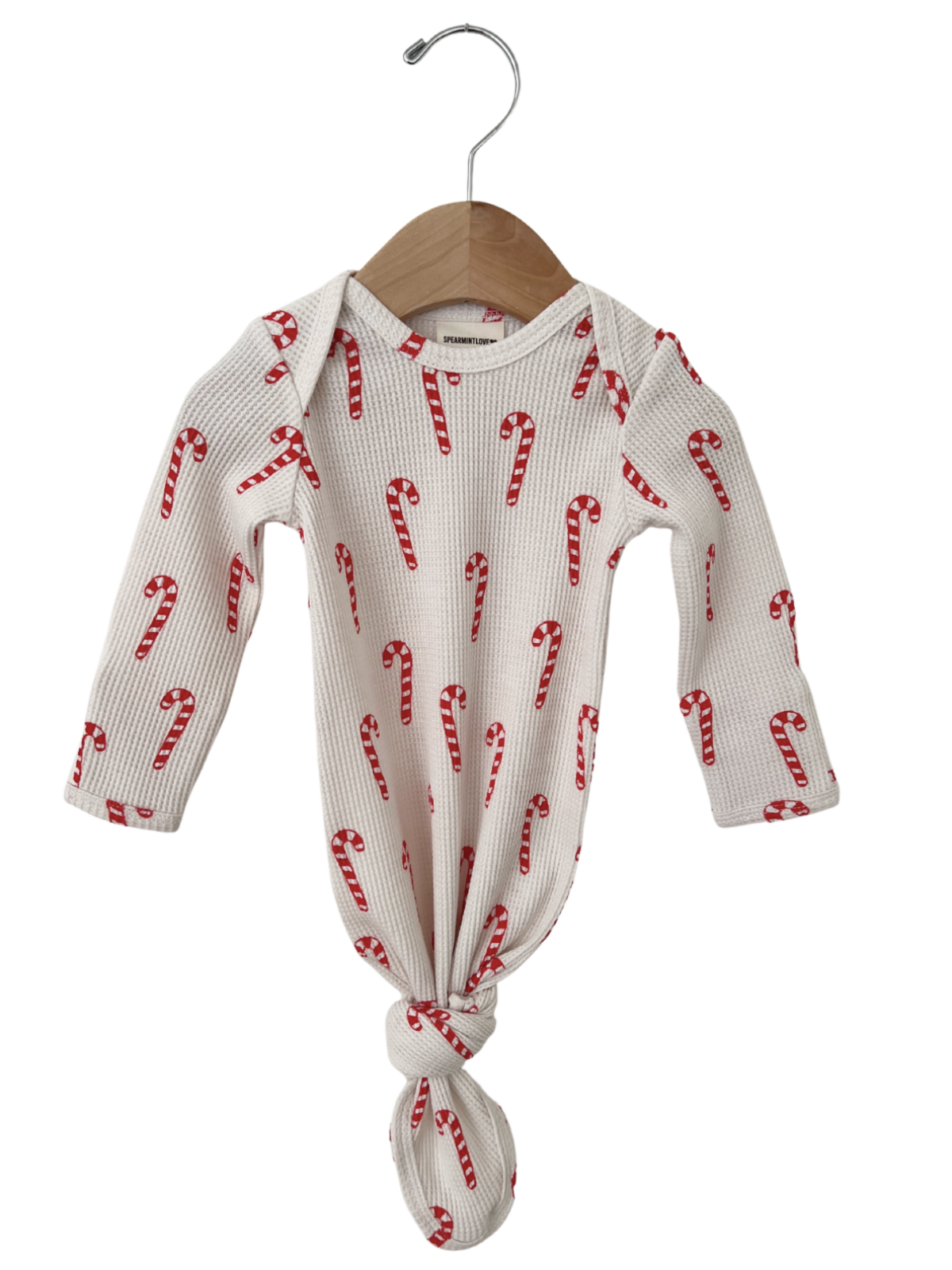 White baby onesie with red candy cane print, tied at the bottom, hanging on a wooden hanger.