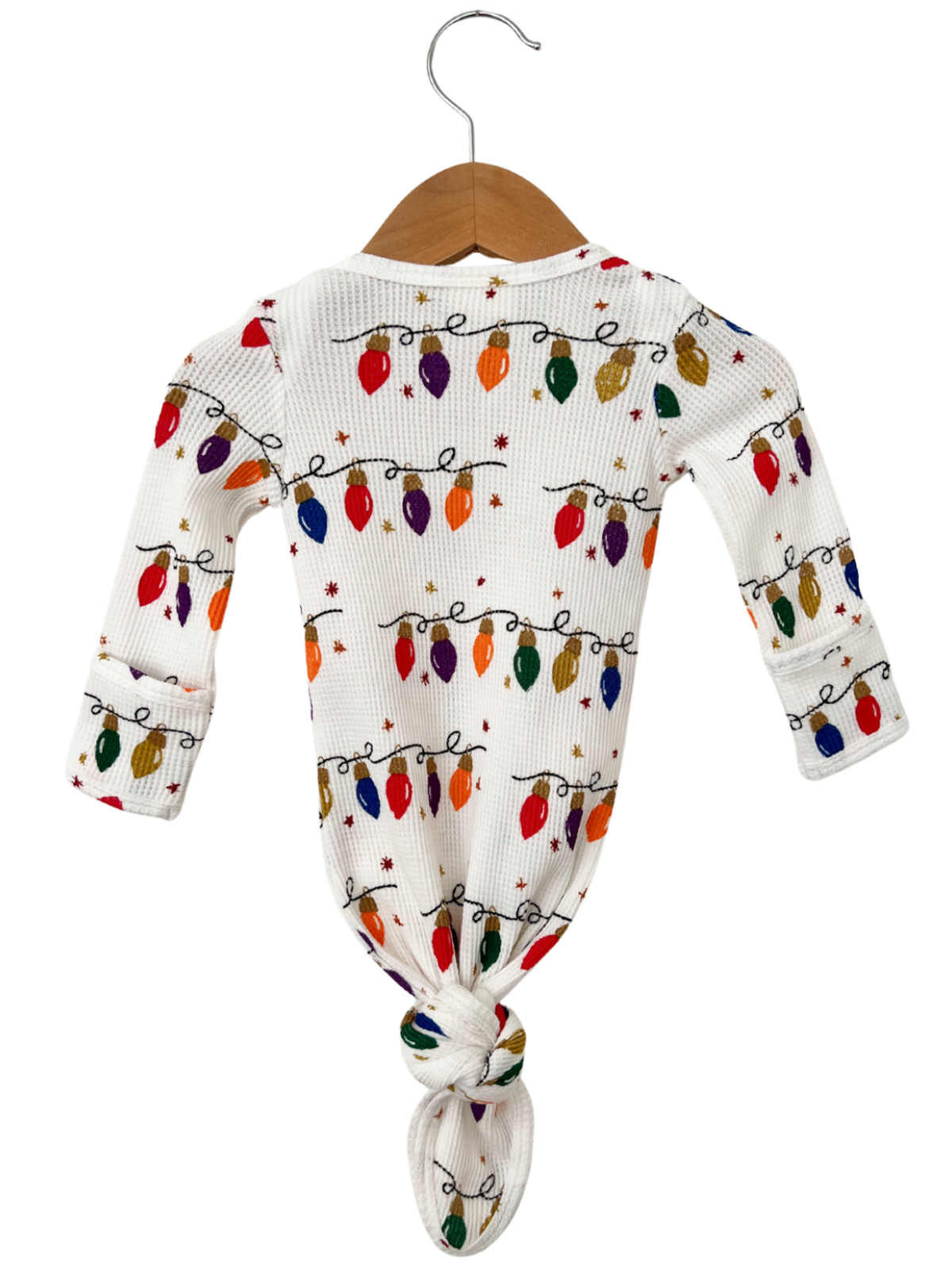 White outfit with colorful Christmas lights pattern, tied at the bottom, hanging on a wooden hanger.