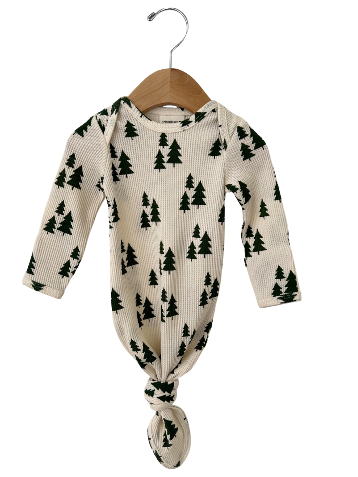 Cream-colored infant outfit with green tree pattern, hung on a wooden hanger.