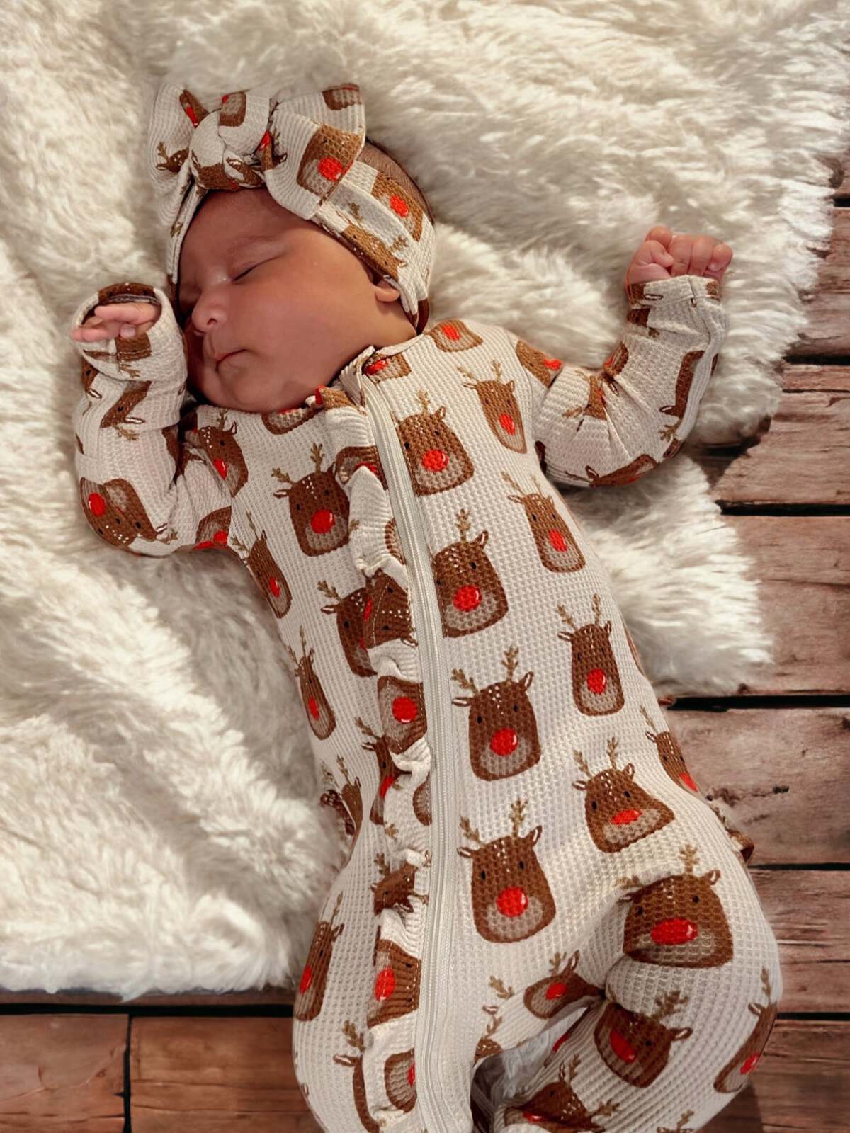 Sleeping baby in reindeer-patterned outfit with matching headband on soft blanket.