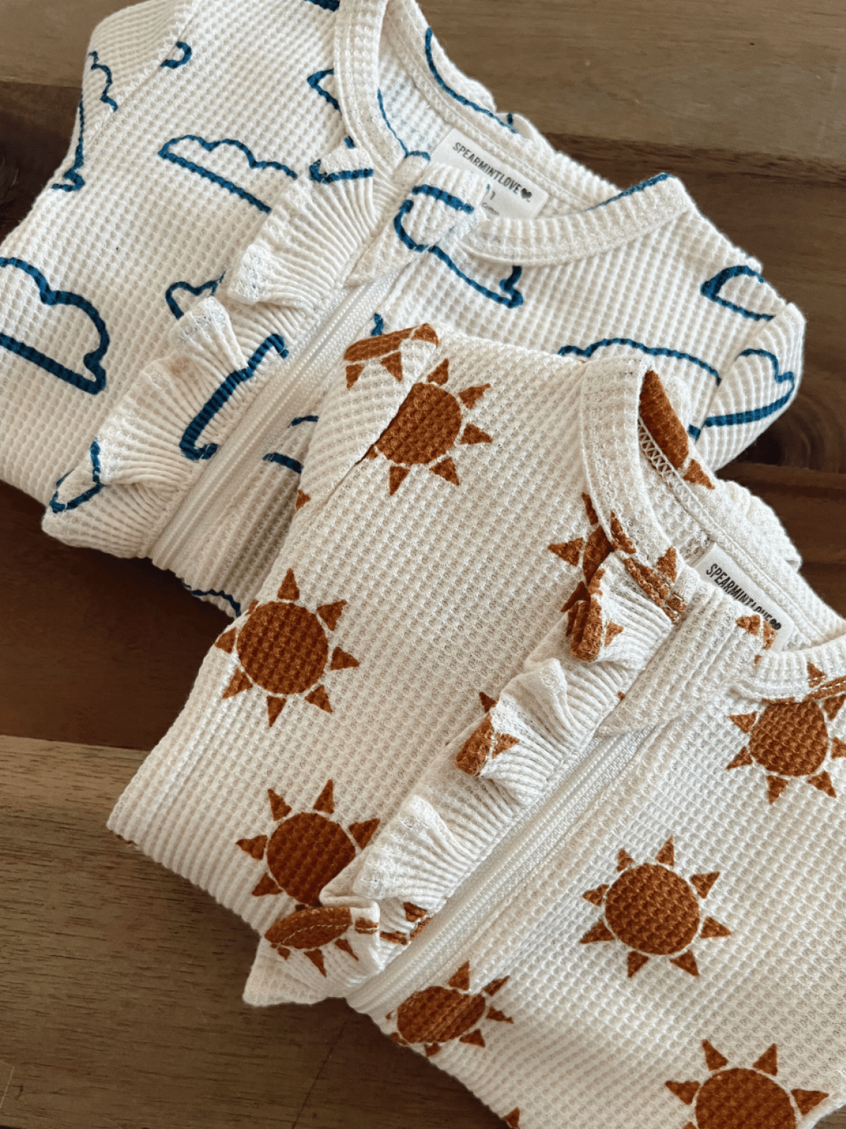 Two cozy toddler outfits with cloud and sun patterns on a wooden surface.