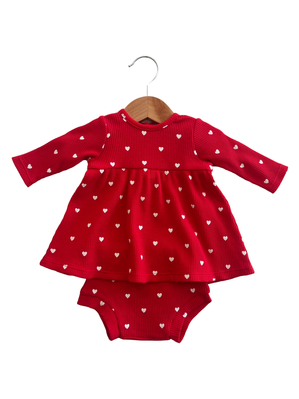 Red dress with white heart patterns, attached bodysuit, hanging on a wooden hanger against a white background.