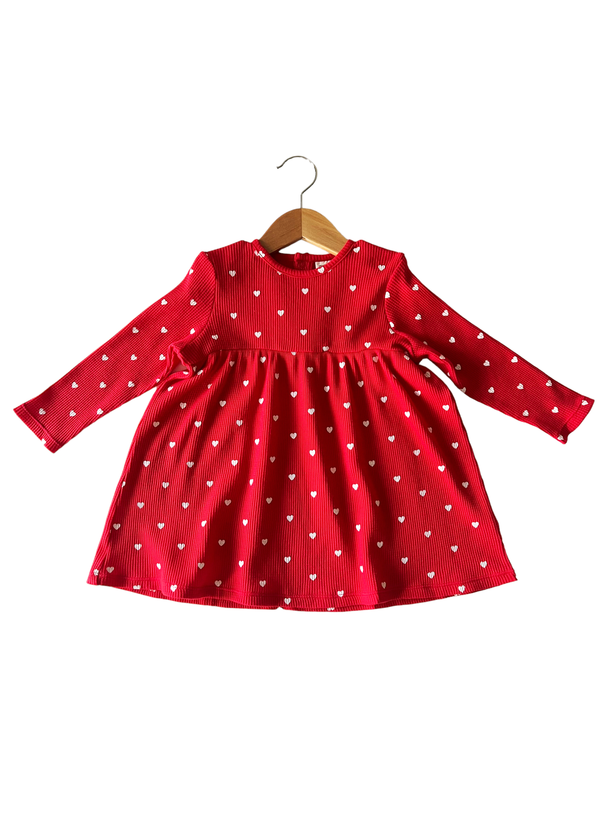 Red dress with long sleeves and white heart patterns, hanging on a wooden hanger.