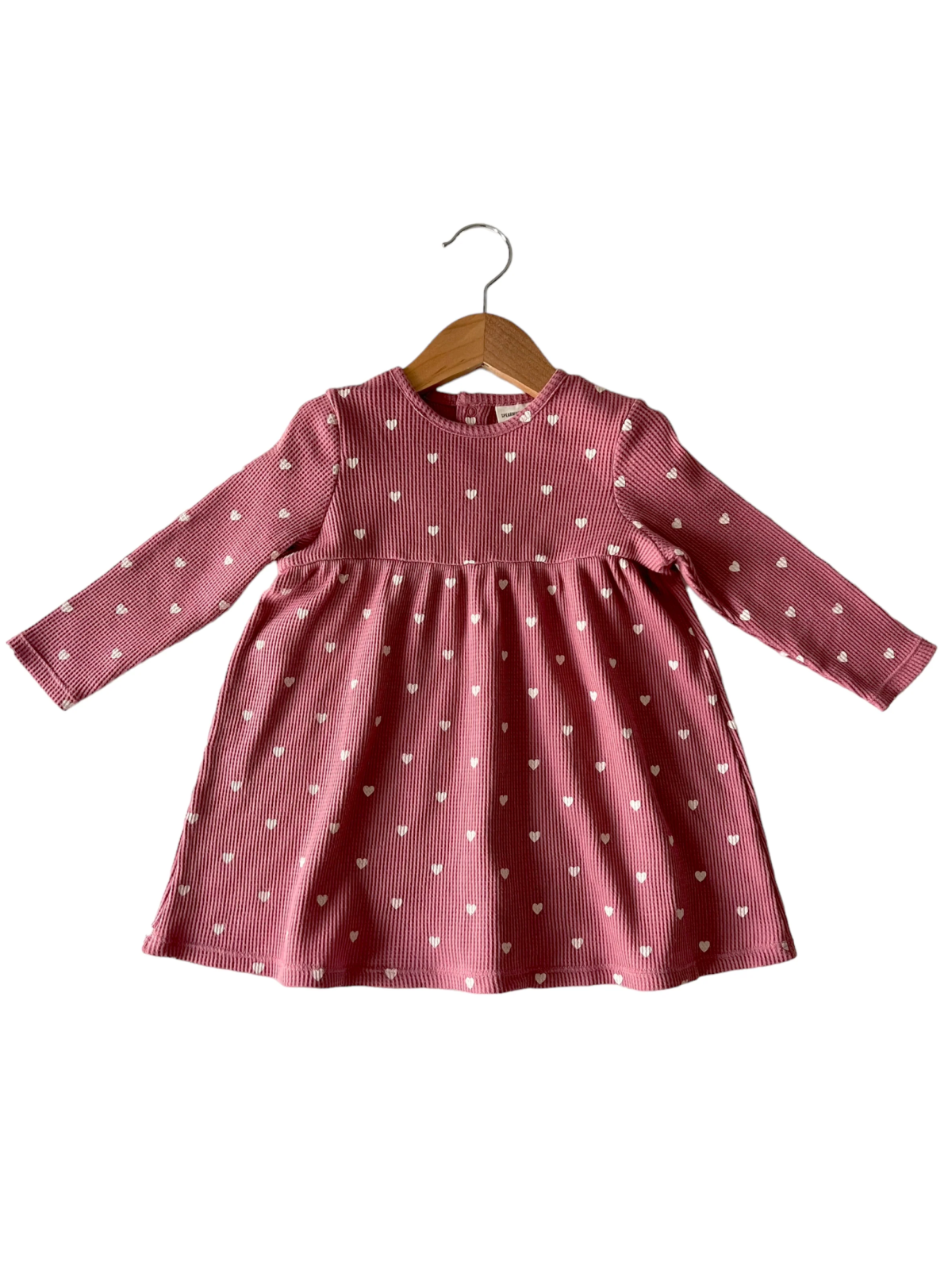 Pink long-sleeve dress with white heart patterns, displayed on a wooden hanger.