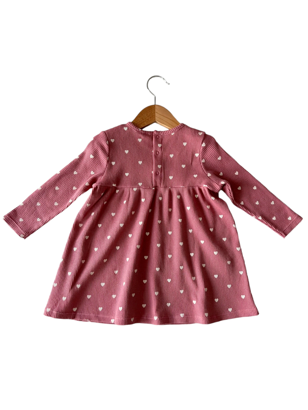 Back view of a pink striped dress with white heart patterns, hanging on a wooden hanger.