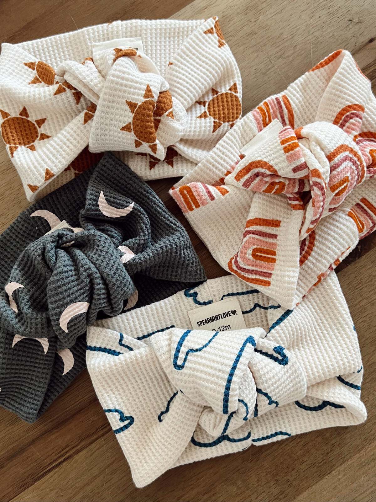 Four colorful fabric headbands with various patterns, including sun and moon designs, on a wooden surface.