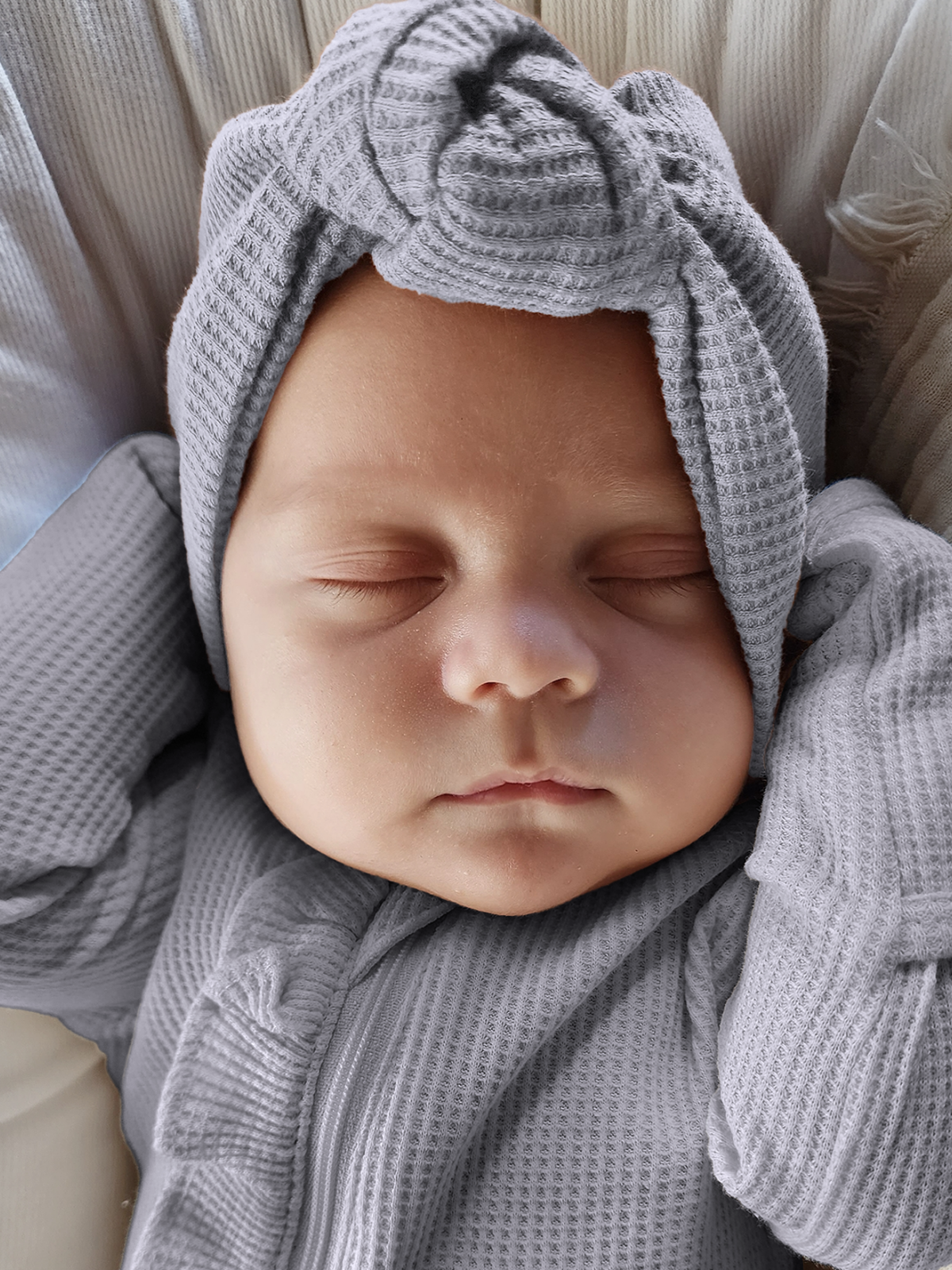 Baby sleeping peacefully in a soft gray outfit with a matching knotted headband.
