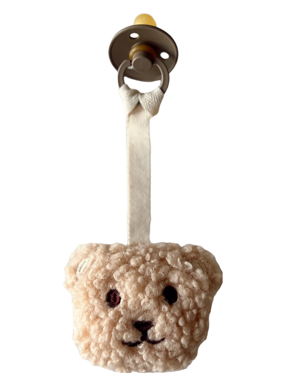 Soft teddy bear pacifier with a plush texture and a fabric strap, ideal for soothing infants.
