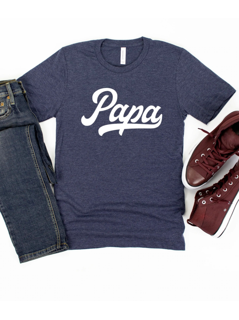 Navy t-shirt with "Papa" in white script, paired with jeans and burgundy sneakers on a white background.