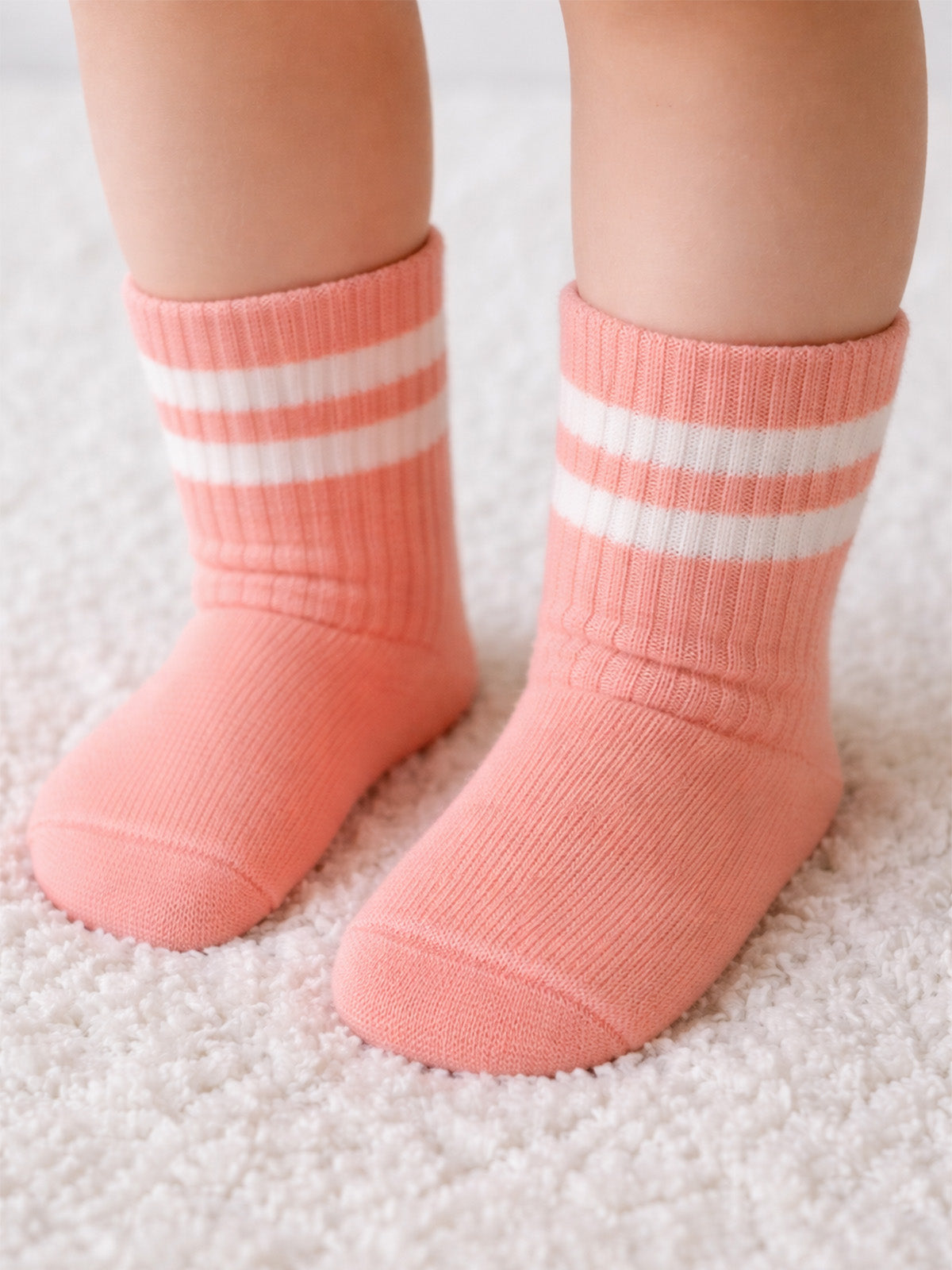 Baby feet in peach socks with white stripes on a soft, fluffy rug.