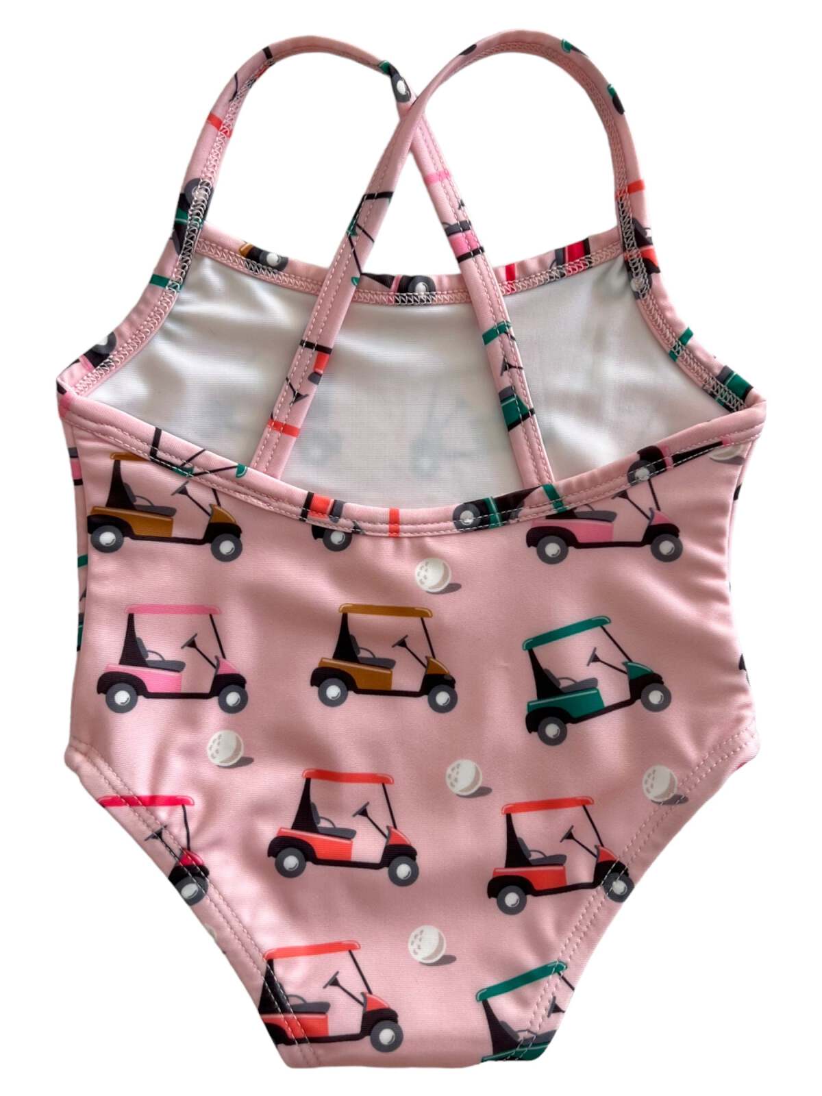 Pink swimsuit with a fun golf cart pattern and white golf balls, featuring crisscross straps.