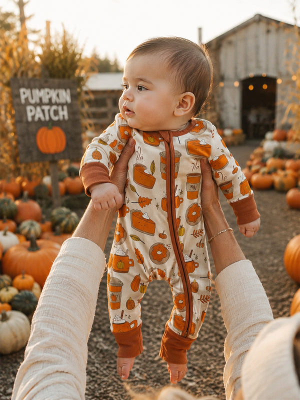 Baby in festive onesie held in a pumpkin patch with pumpkins and a “Pumpkin Patch” sign in the background.