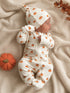 Newborn in pumpkin-printed outfit on a cozy blanket, next to a felt pumpkin and autumn leaves.