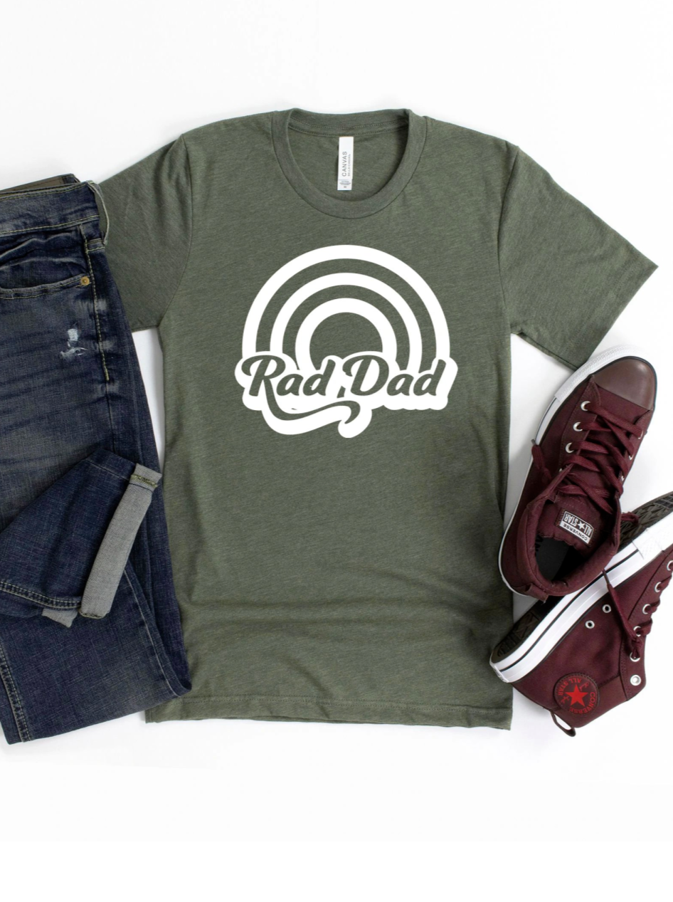 Green "Rad Dad" t-shirt styled with blue jeans and maroon sneakers on a white background.