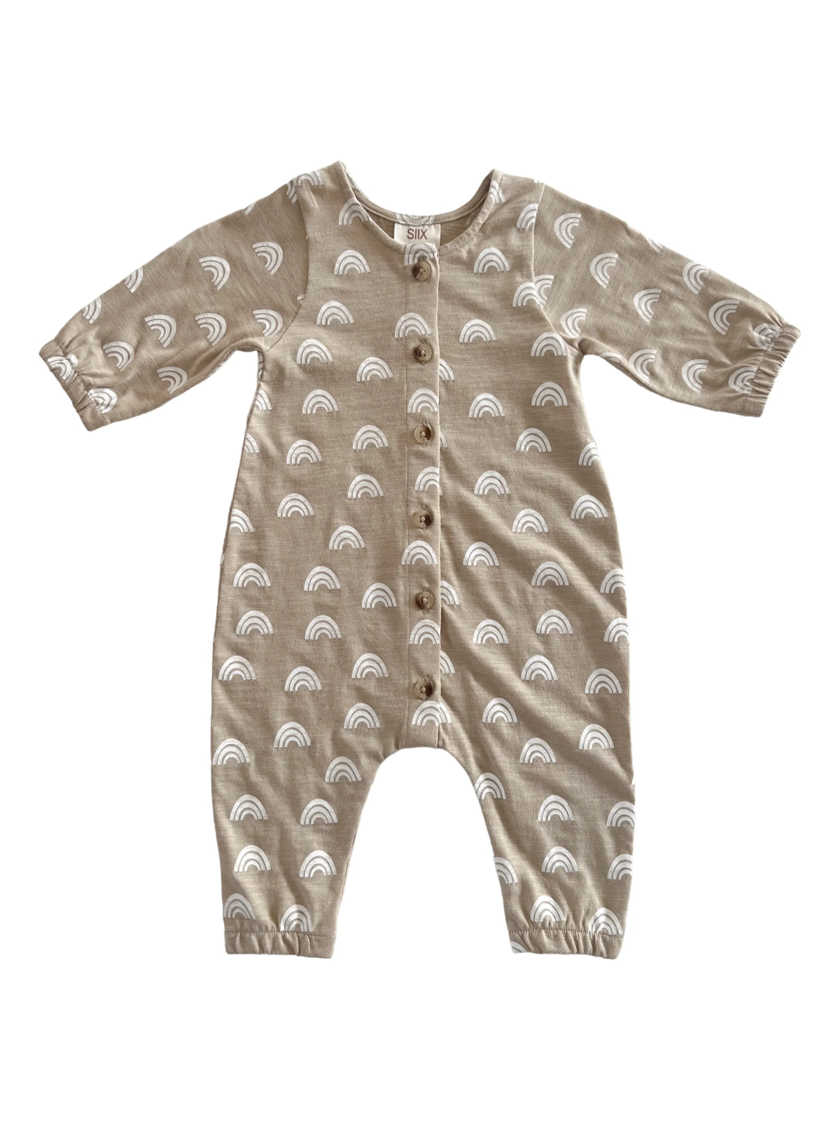 Beige toddler jumpsuit with white rainbow patterns and buttons down the front. Long sleeves and relaxed fit.