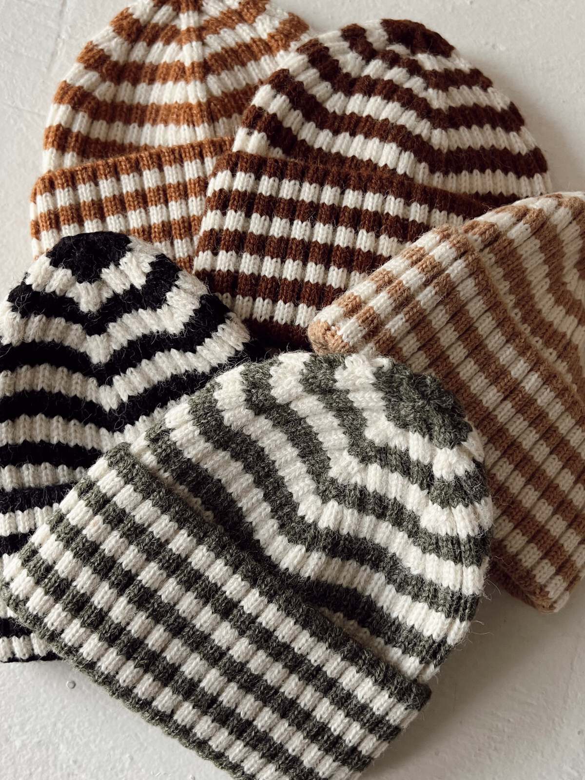 Collection of striped knit beanie hats in various colors, arranged together on a light background.