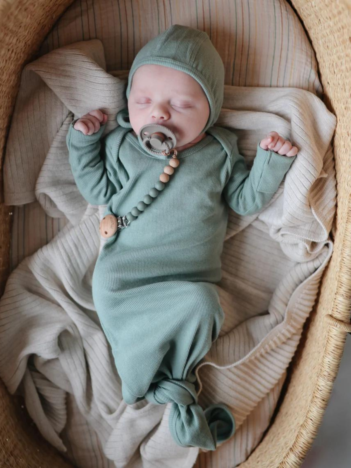 A sleeping baby in a green outfit, swaddled in cozy blankets, resting in a woven basket.