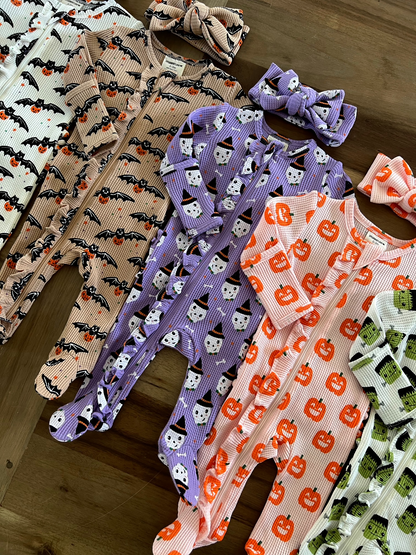 Colorful baby onesies with Halloween themes, featuring bats, pumpkins, and ghosts, arranged with matching headbands.