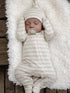 Sleeping baby in a striped outfit and hat, nestled on a fluffy white blanket.