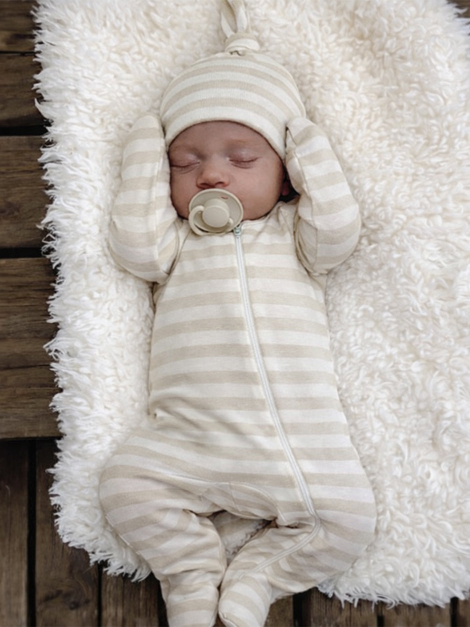 Sleeping baby in a striped outfit and hat, nestled on a fluffy white blanket.