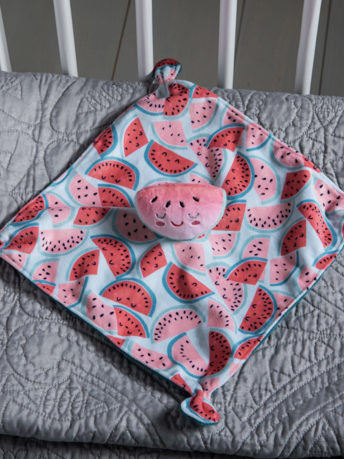 Colorful baby blanket featuring a watermelon design, resting on a textured gray surface.
