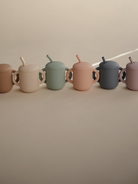 A row of six colorful, matte finish cups with straws, displayed on a beige background.