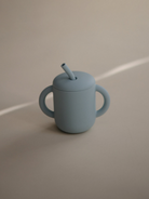 Light blue cup with two handles and a straw, positioned on a neutral surface.
