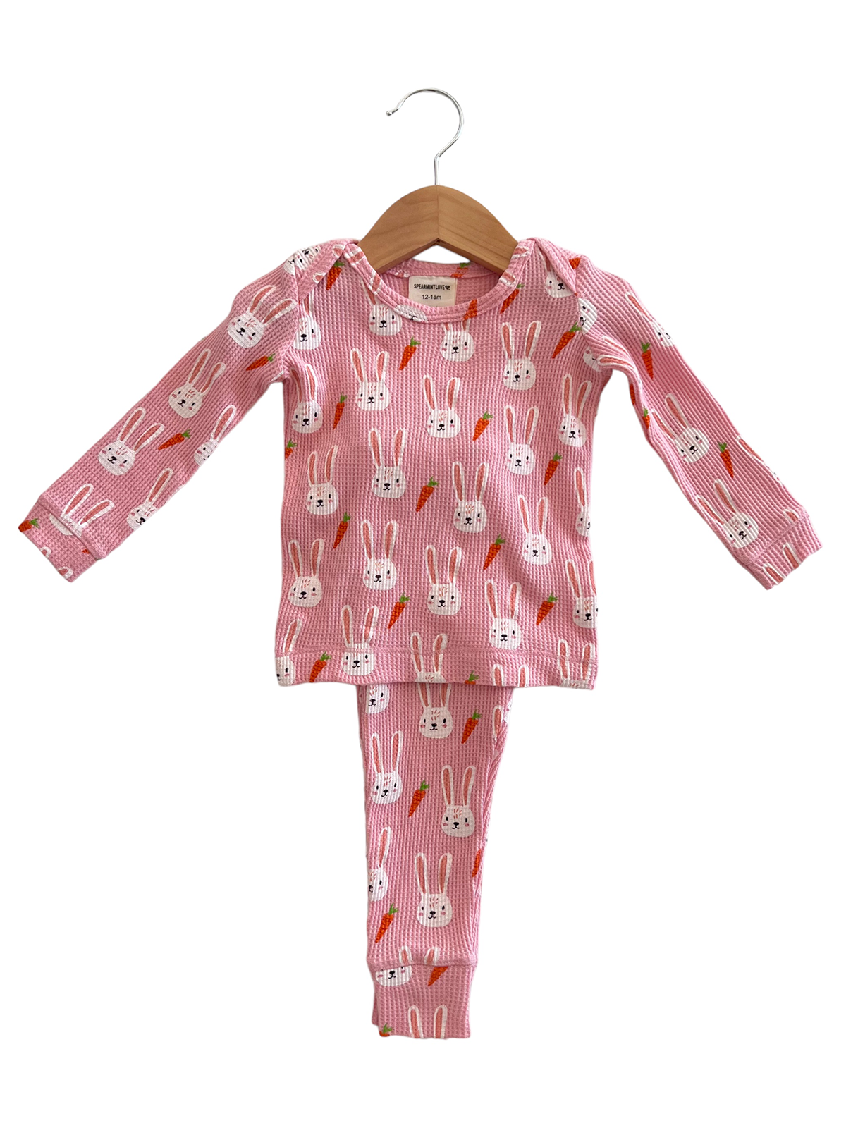 Pink bunny-patterned toddler pajama set with long sleeves and pants, hanging on a wooden hanger.