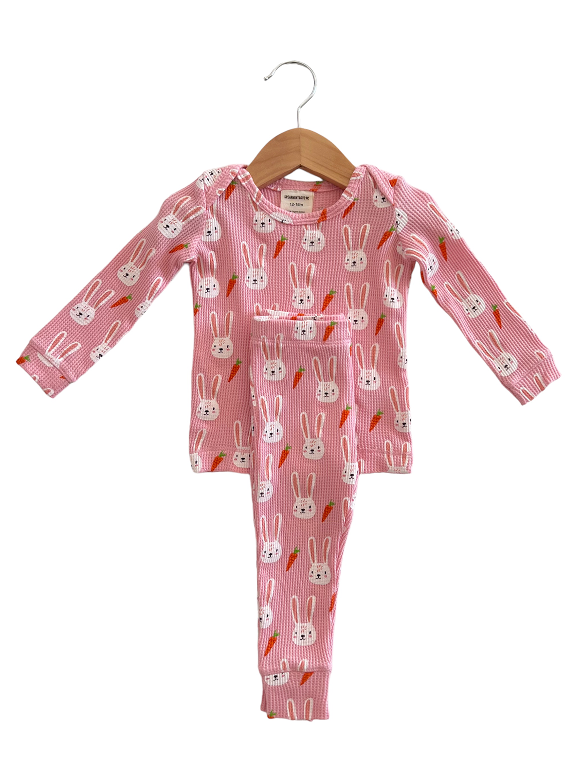 Pink children's pajama set featuring bunny and carrot designs, displayed on a wooden hanger.