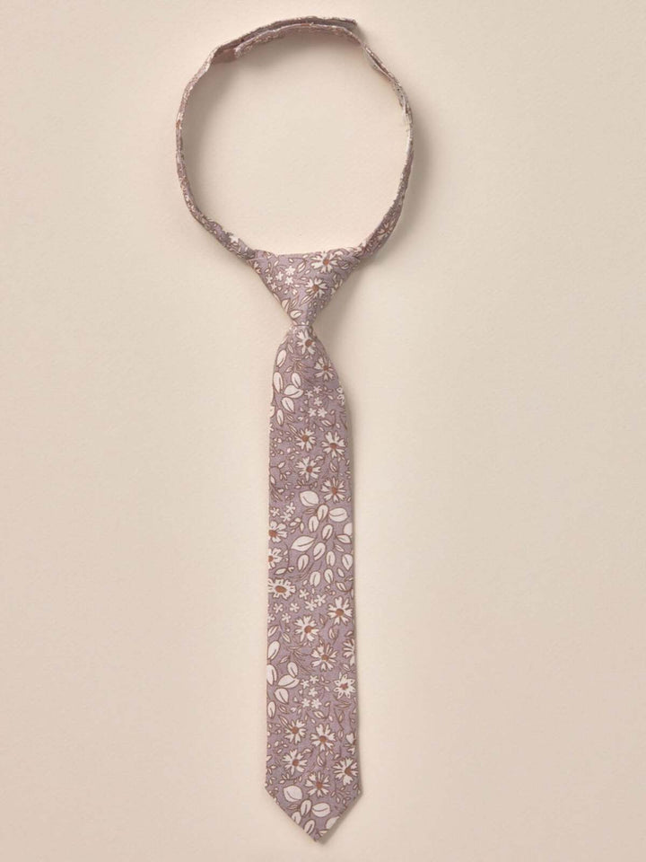 Floral patterned tie hanging against a neutral background, showcasing delicate leaves and blossoms.