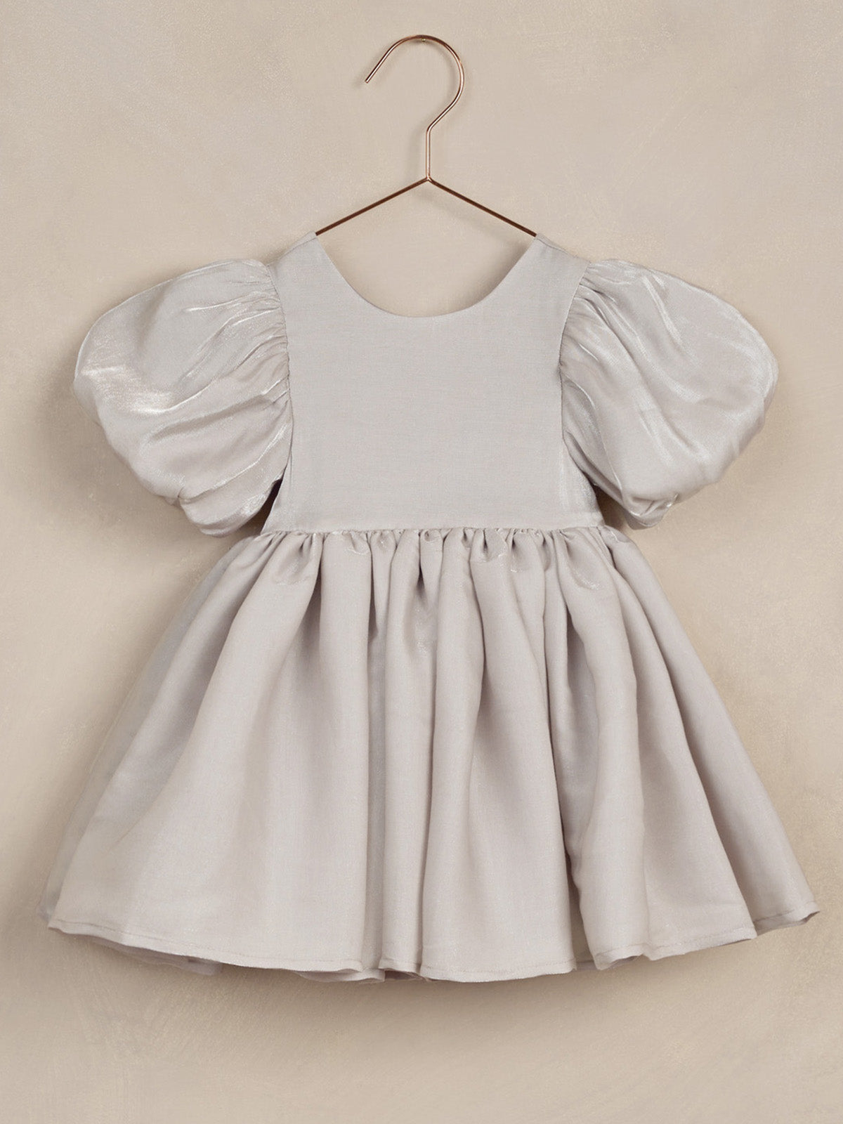 Pale gray dress with puff sleeves, hanging on a rose gold hook against a beige background.