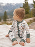 Toddler in nature-themed pajamas sitting on a blanket with mountains in the background.