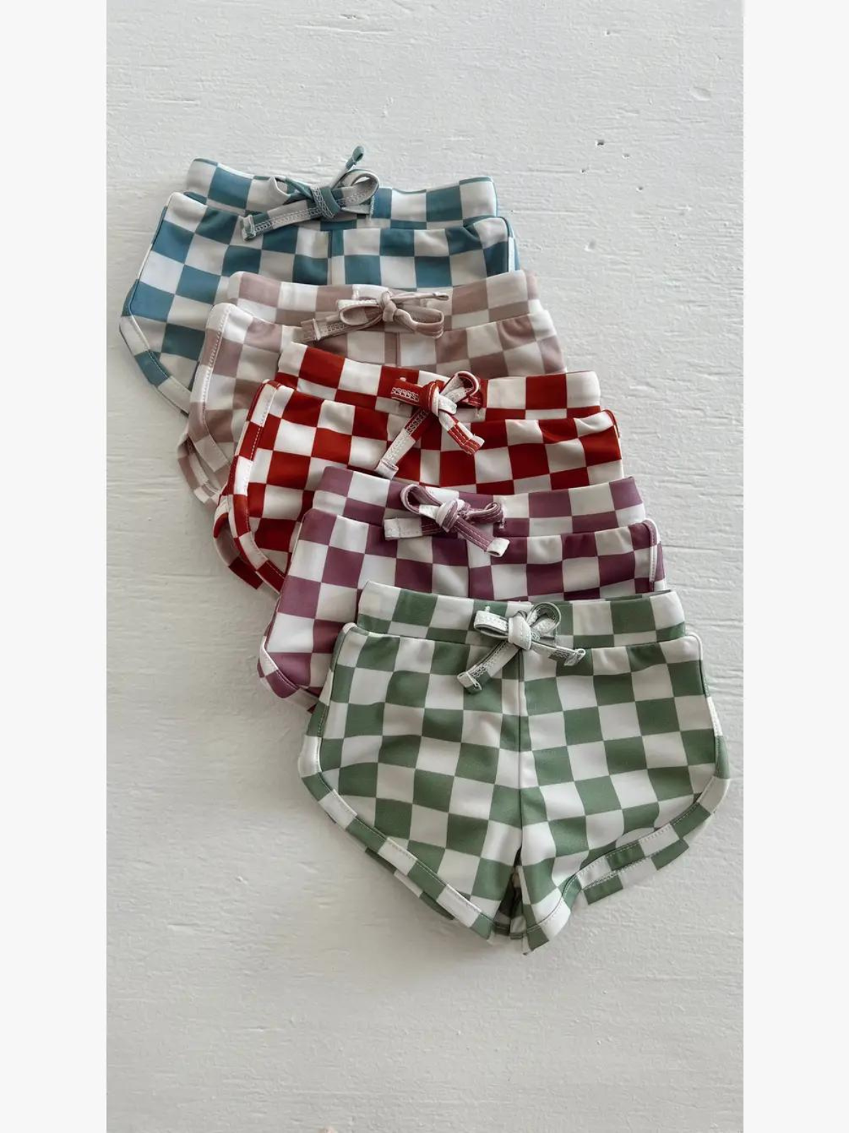 Five pairs of checkered shorts in blue, purple, red, and green arranged neatly on a white background.