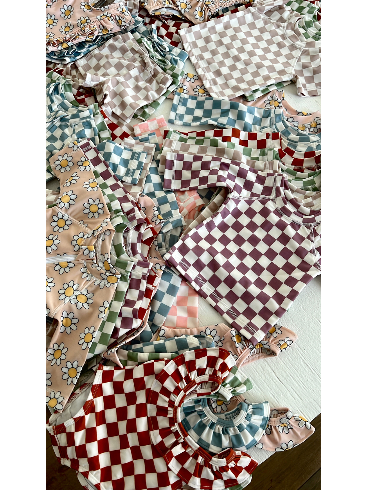 Colorful children's clothing featuring floral patterns and checkered designs scattered on a surface.