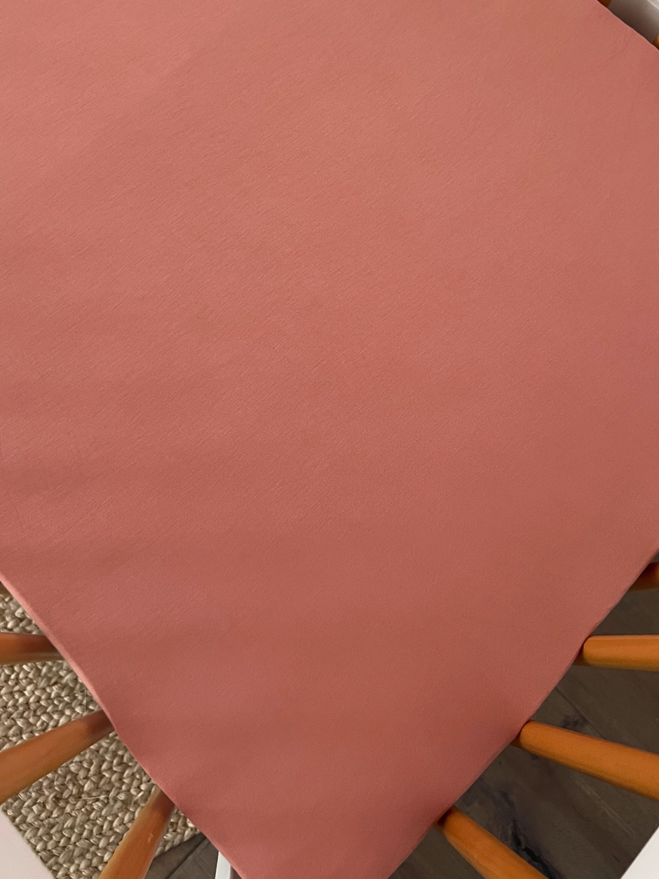 Solid coral-colored fabric draped over a chair, showcasing a soft texture and modern decor.