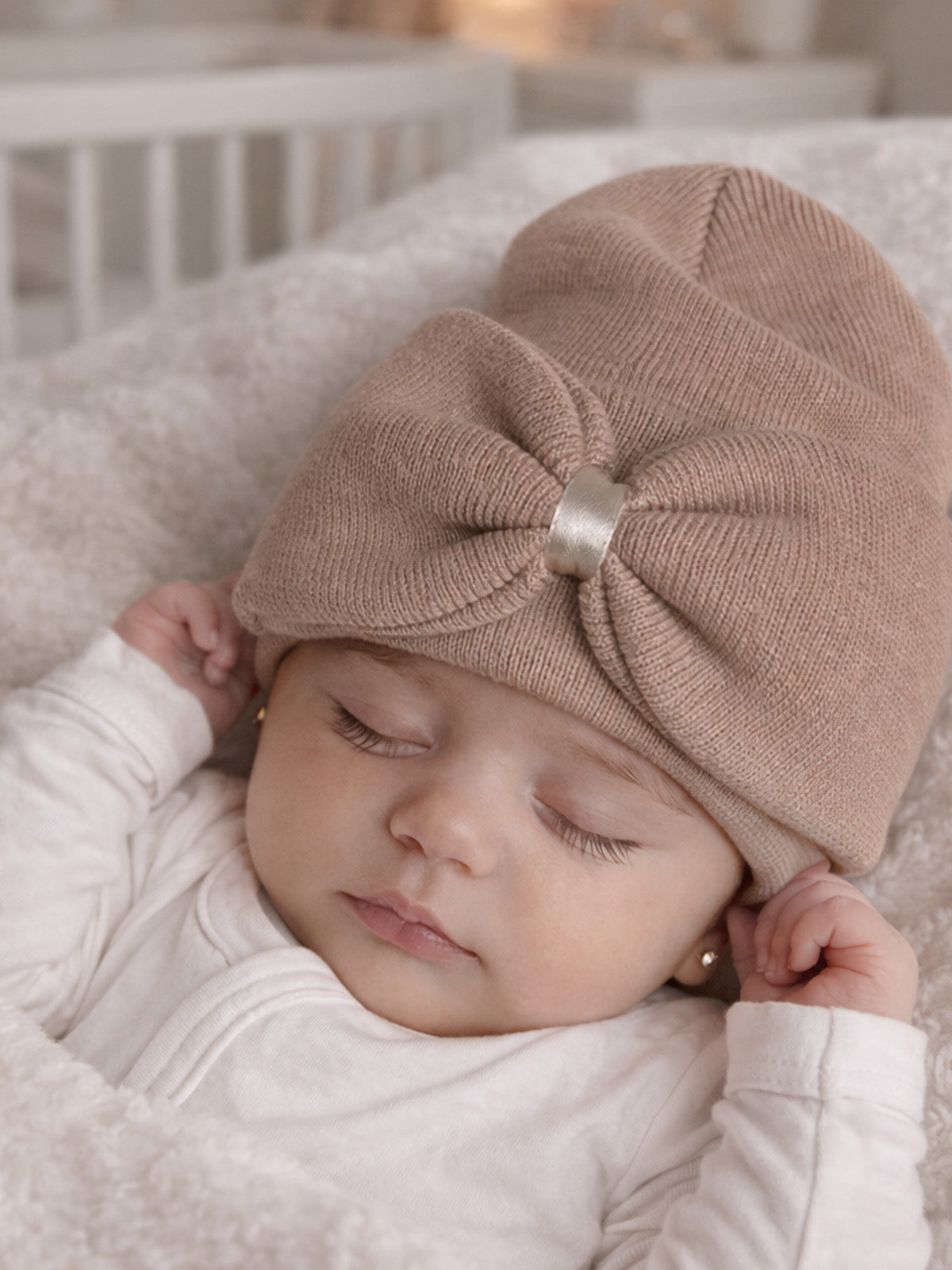 Baby girl peacefully sleeping in a cozy blanket, wearing a knit hat with a bow. Soft, neutral colors.