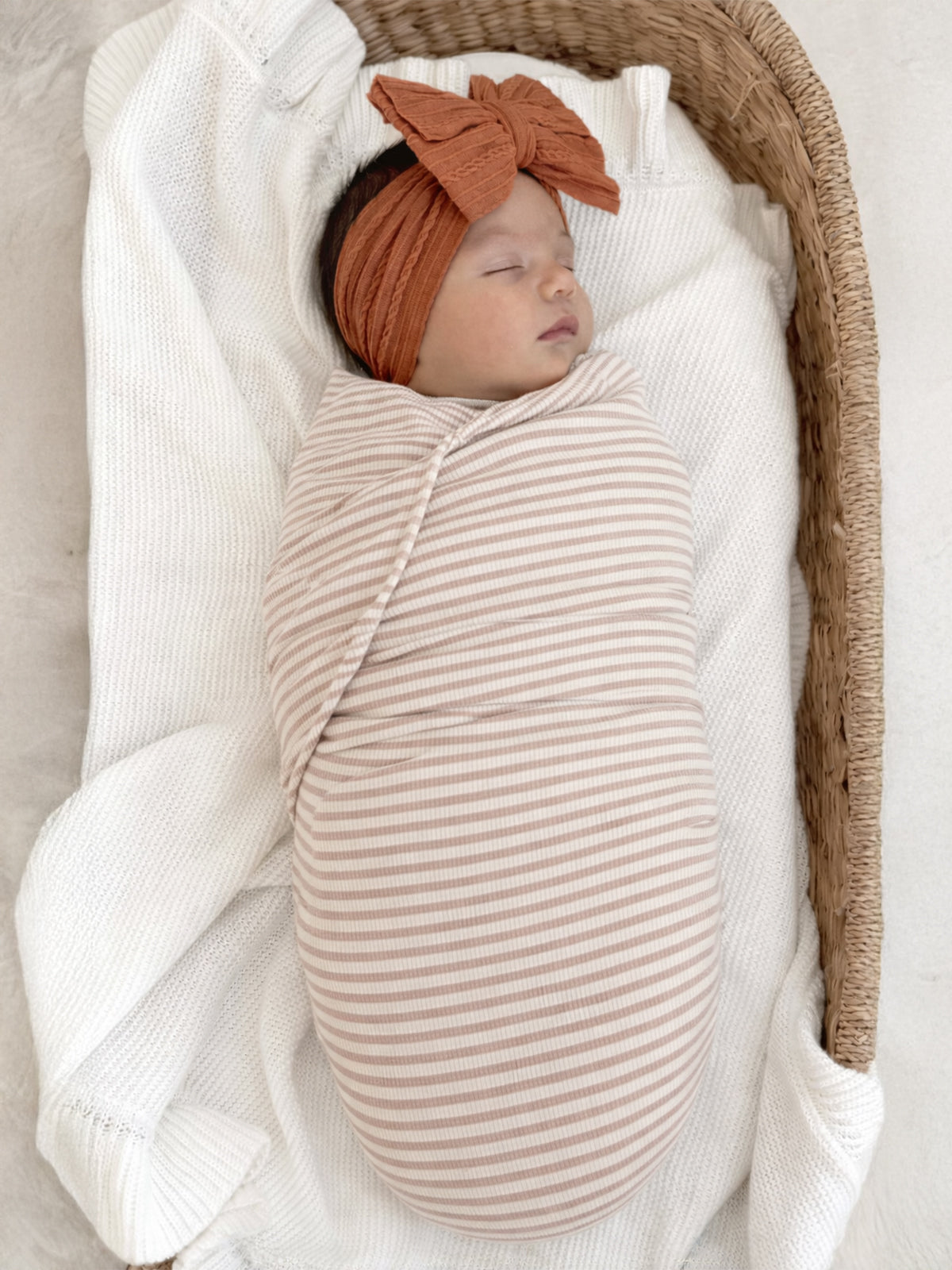 Newborn wrapped in a striped blanket, peacefully sleeping in a cozy basket with a soft knit blanket.