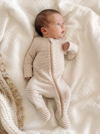 Baby in a striped sleeper lies on a soft blanket, looking up with a curious expression.