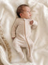 Baby in a striped sleeper lies on a soft blanket, looking up with a curious expression.