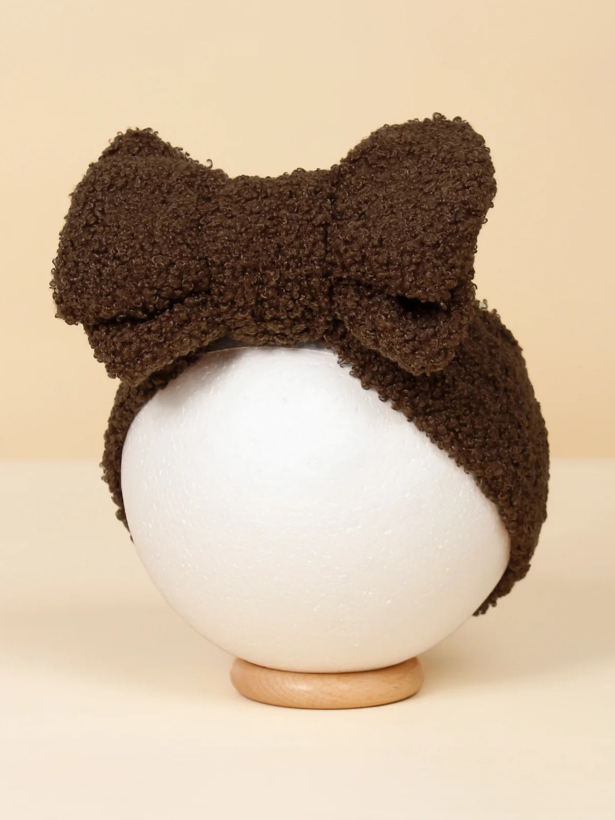 Brown textured headband with a large bow displayed on a white stand against a soft beige background.