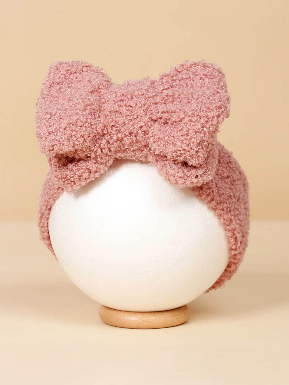 Pink textured headband with a large bow, displayed on a white round stand against a neutral background.
